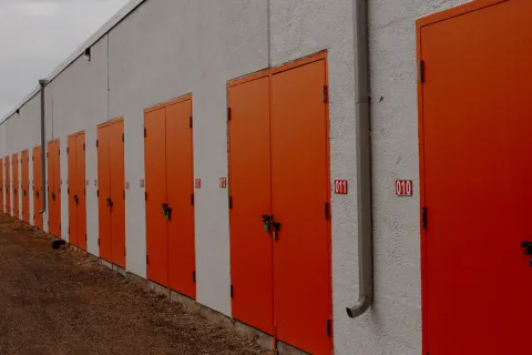 A row of outdoor self-storage units with bright orange doors and red unit number signs outdoors