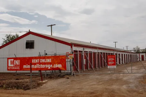 Outdoor drive-up self-storage facility with white buildings, red trim, and a chain-link security gate turn-around