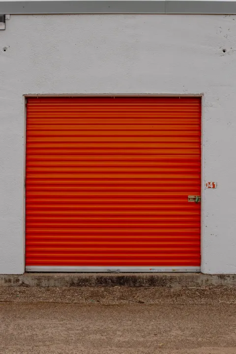 An orange roll-up storage unit door numbered 041 set into a white exterior wall