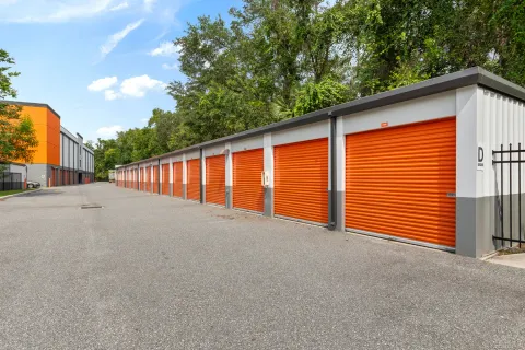 A row of drive-up self-storage units with orange roll-up doors along a paved outdoor driveway