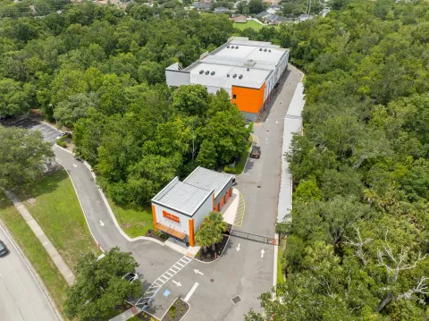 Aerial view of a multi-story self-storage facility with orange accents, a gated entrance, and surrounding trees