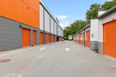 Rows of orange roll-up storage unit doors line a paved drive with directional arrows and a truck