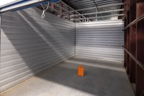 An empty indoor storage unit with corrugated metal walls and a single orange bag on the floor