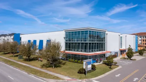 A modern multi-story self-storage building with large glass windows and an orange awning under a blue sky