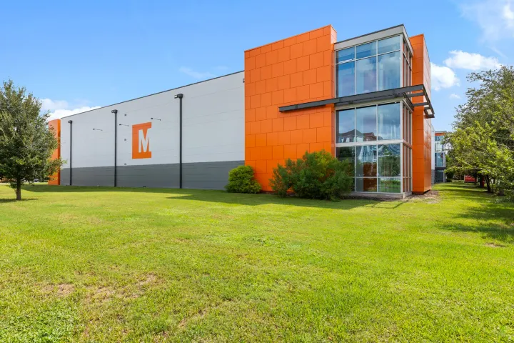 Exterior of a modern multi-story storage building with orange panels, large windows, and a grassy field