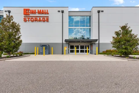 Exterior view of Mini Mall Storage building featuring glass entrance doors, yellow bollards, and Amazon locker