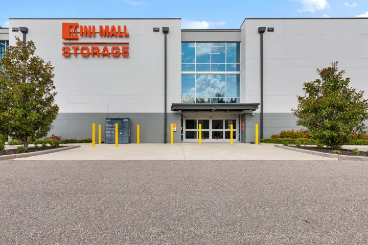 Exterior view of Mini Mall Storage building featuring glass entrance doors, yellow bollards, and Amazon locker