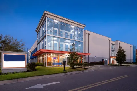 Multi-story storage facility exterior with a glass-front office and orange overhang at twilight