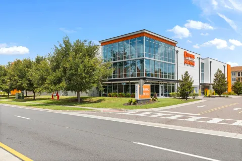 Multi-story glass storage facility with orange signage and manicured lawn located next to a paved road