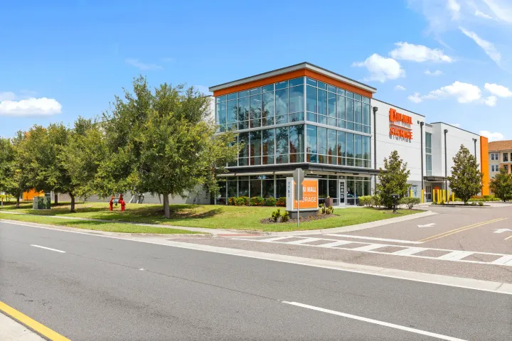 Multi-story glass storage facility with orange signage and manicured lawn located next to a paved road