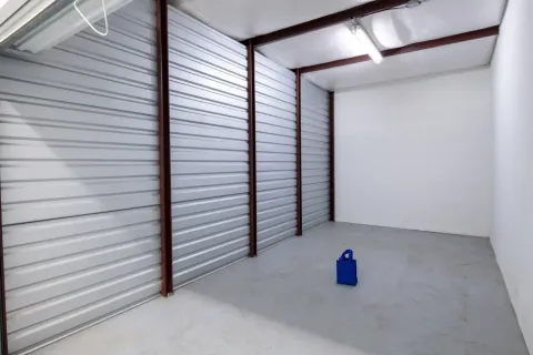 Interior of a large empty storage unit with corrugated metal walls and a single blue bag