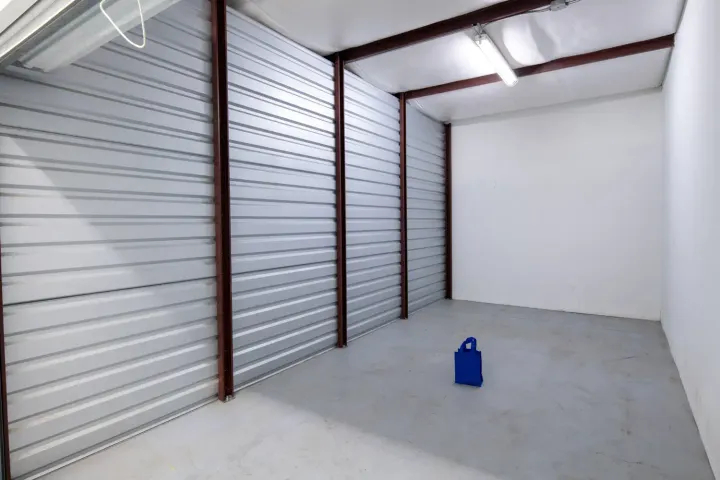 Interior of a large empty storage unit with corrugated metal walls and a single blue bag