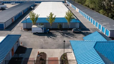 Aerial view of storage buildings with blue roofs and a moving truck parked in the paved lot