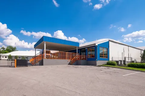 Blue storage facility office with a covered loading dock, orange railings, and a paved parking lot