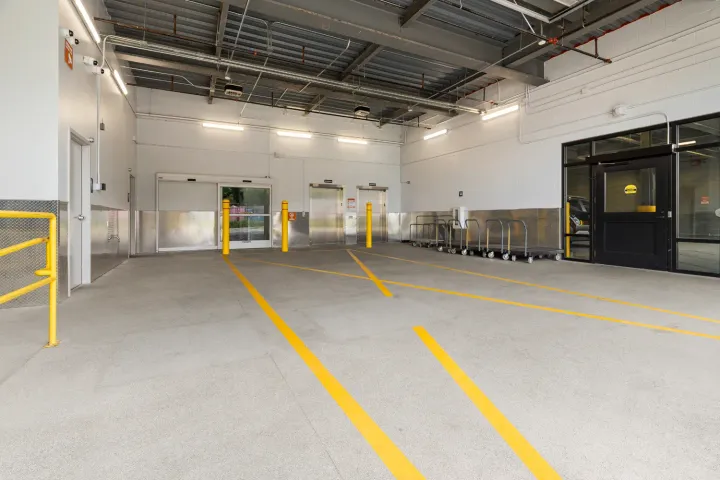 Indoor loading bay with elevators, sliding glass doors, yellow bollards, and rows of flatbed moving carts