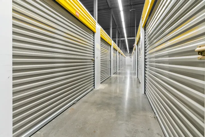 An indoor storage hallway with polished concrete floors and rows of gray roll-up doors with yellow trim