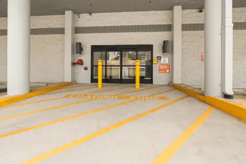 Covered loading zone with yellow painted lines leading to glass sliding doors and two yellow bollards