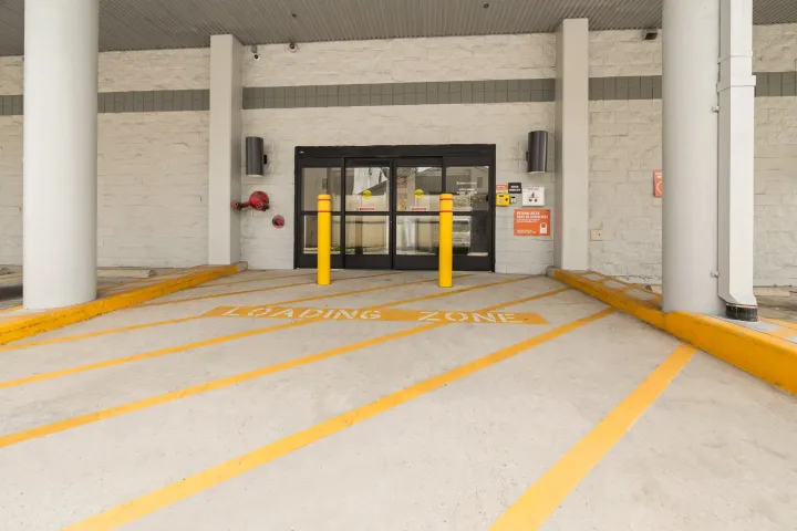Covered loading zone with yellow painted lines leading to glass sliding doors and two yellow bollards