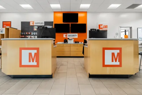 Modern storage office interior featuring wood reception counters, security monitors, and a packing supplies display wall