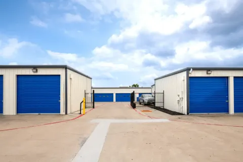 Drive-up self-storage buildings with blue roll-up doors and an open black metal security gate