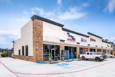 Exterior of a retail strip mall with stone accents, storefront signage, and a paved parking lot