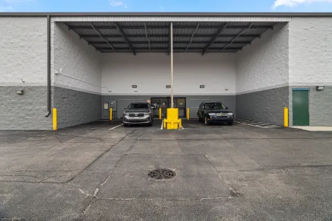 A covered loading area with two cars parked in front of glass doors and yellow bollards