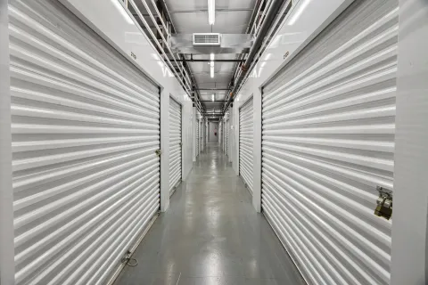 Indoor storage facility hallway featuring bright white corrugated roll-up doors and a polished gray floor