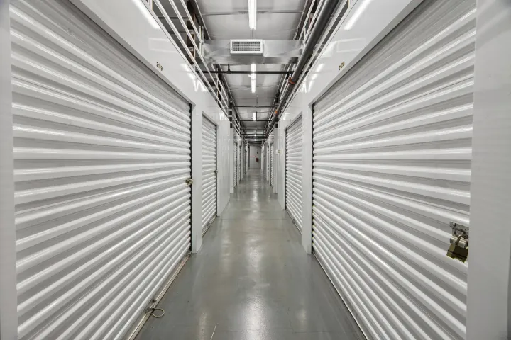 Indoor storage facility hallway featuring bright white corrugated roll-up doors and a polished gray floor