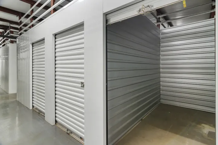 White indoor storage units with corrugated metal roll-up doors and one open unit showing metal interior walls