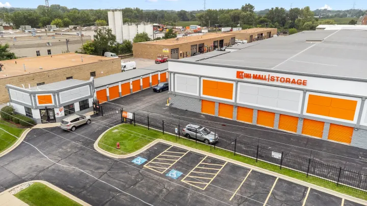 High angle view of Mini Mall Storage buildings with orange roll-up doors and a gated entrance