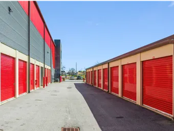 Wide asphalt driveway between drive-up storage units in North Augusta on Cork Tree Bend with red roll-up doors leading toward a gated entrance under clear skies