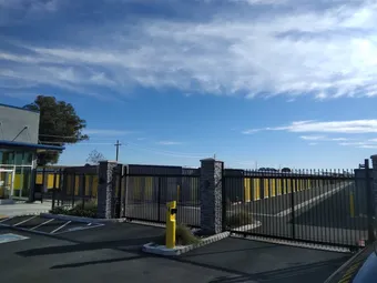 Entrance gate to the storage facility with fence and yellow unit doors visible.