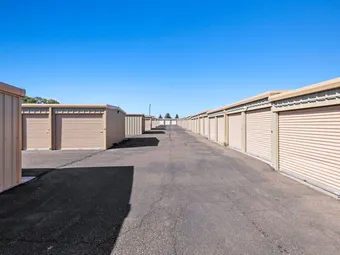 Outdoor storage units with roll-up doors along a paved driveway.