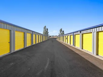 Open outdoor hallway between two rows of self-storage units with yellow doors.