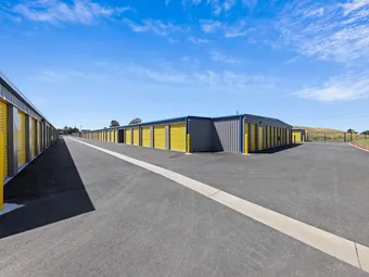 Long driveway between rows of outdoor storage units with yellow doors.