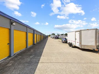 Row of outdoor storage units with yellow doors and parking for vehicles