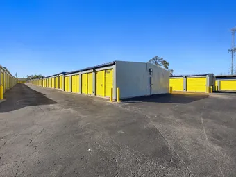 Outdoor drive-up storage units with yellow doors and a cell tower.