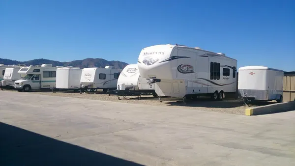 Several recreational vehicles and white trailers parked in an outdoor storage lot under a clear blue sky