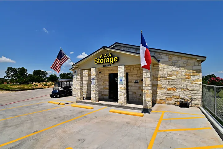 Stone office building with A-A-A Storage signage, flags, a golf cart, and a paved parking lot