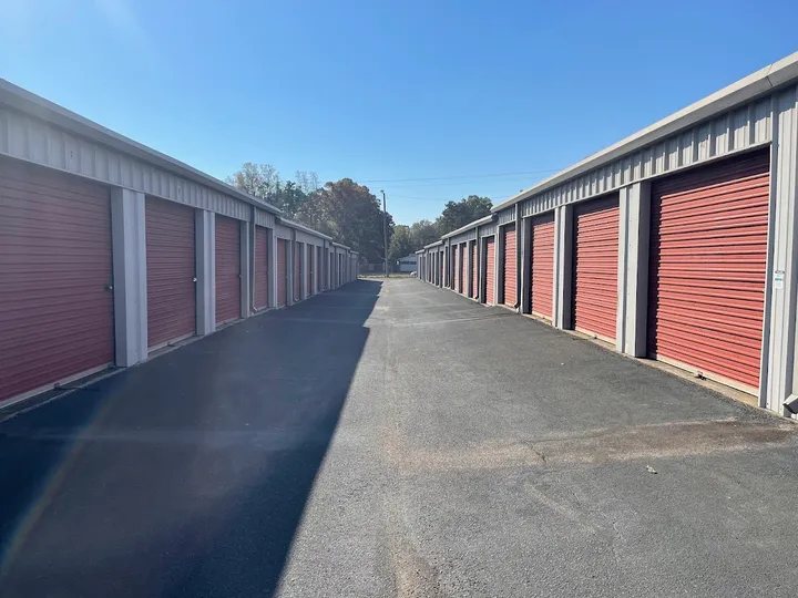 Wide asphalt driveway between two long rows of tan buildings with red roll-up storage doors