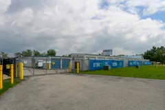 A metal gate leading to drive-up storage units with blue StorSafe banners and yellow bollards