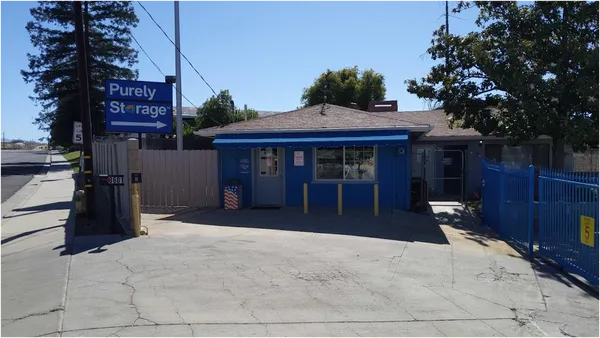 Exterior view of a blue Purely Storage office building with a paved driveway and metal fencing