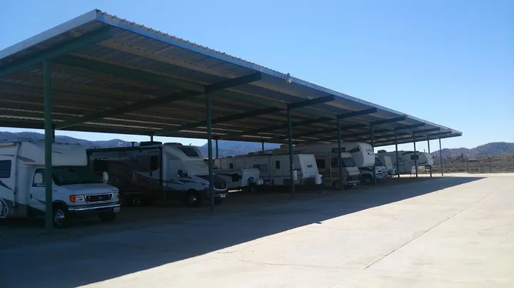 Large outdoor storage area with multiple RVs and campers parked under a long metal canopy roof