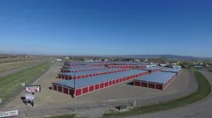 High angle view of a fenced self-storage facility with long rows of red drive-up units and signage
