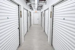 A well-lit indoor storage hallway with white corrugated unit doors, number signs, and ceiling air ducts