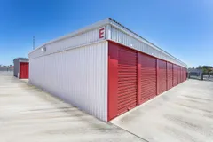 Exterior view of drive-up self-storage units with white metal siding and red roll-up doors