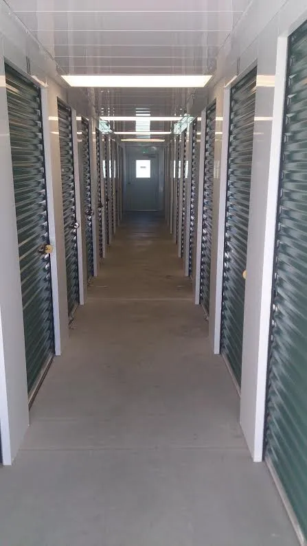 Brightly lit indoor storage hallway with rows of green corrugated metal doors and white trim