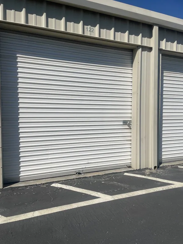 White roll-up storage unit door number 122 at a drive-up facility with asphalt and parking lines
