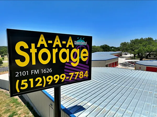 A large sign for A-A-A Storage stands above metal rooftops and drive-up storage buildings under a clear sky