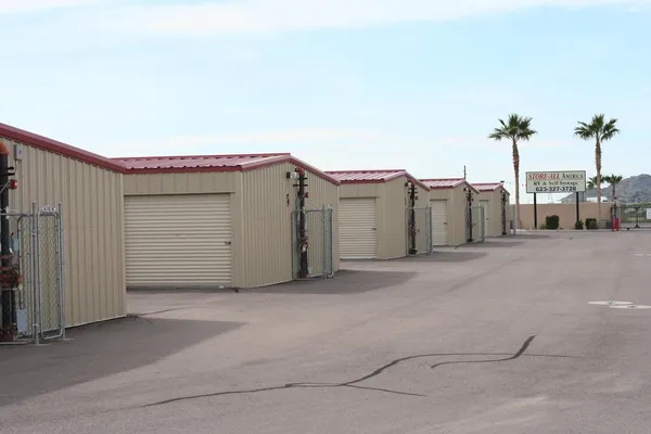 Row of tan drive-up storage units with red roofs and a Store-All America sign near palm trees